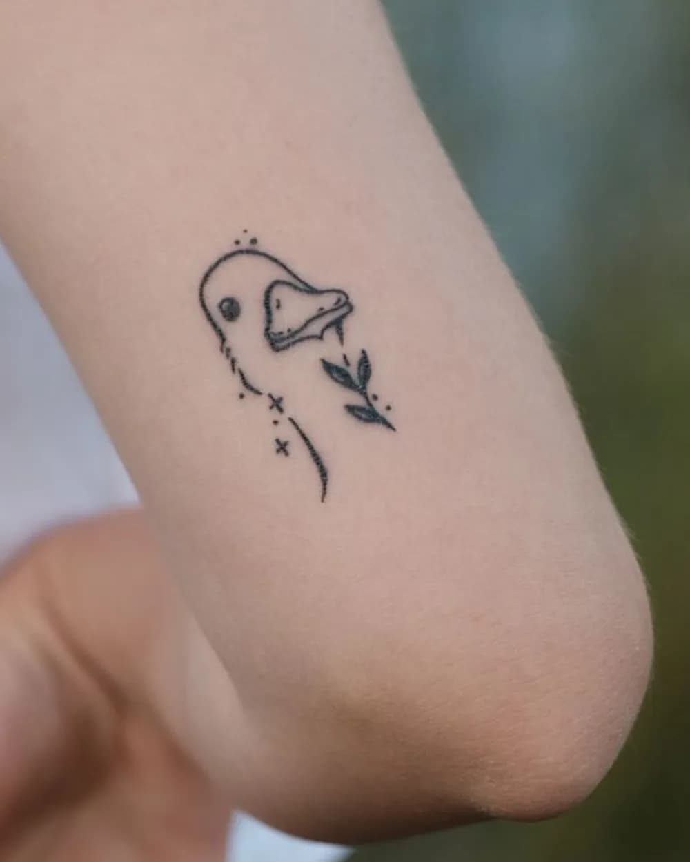 Small fine-line duck tattoo photographed clearly on the back of an upper arm