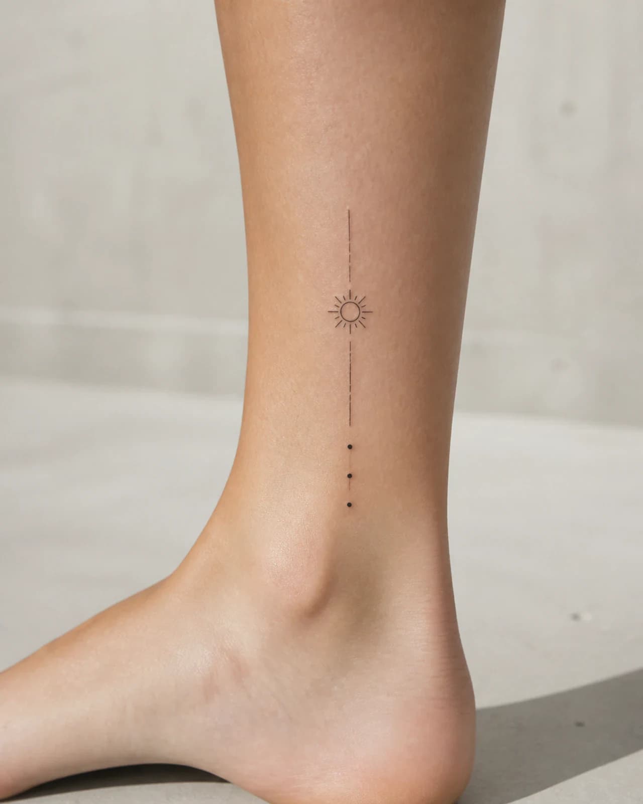 Vertical fine line sun path with small orbit dots tattooed beside an adult ankle bone