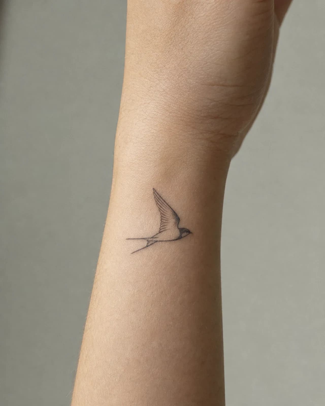 Tiny fine line swallow tattoo in flight on the outer side of an adult wrist