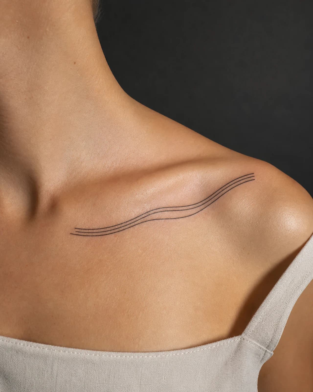 Abstract parallel contour ribbon fine line tattoo tracing an adult collarbone