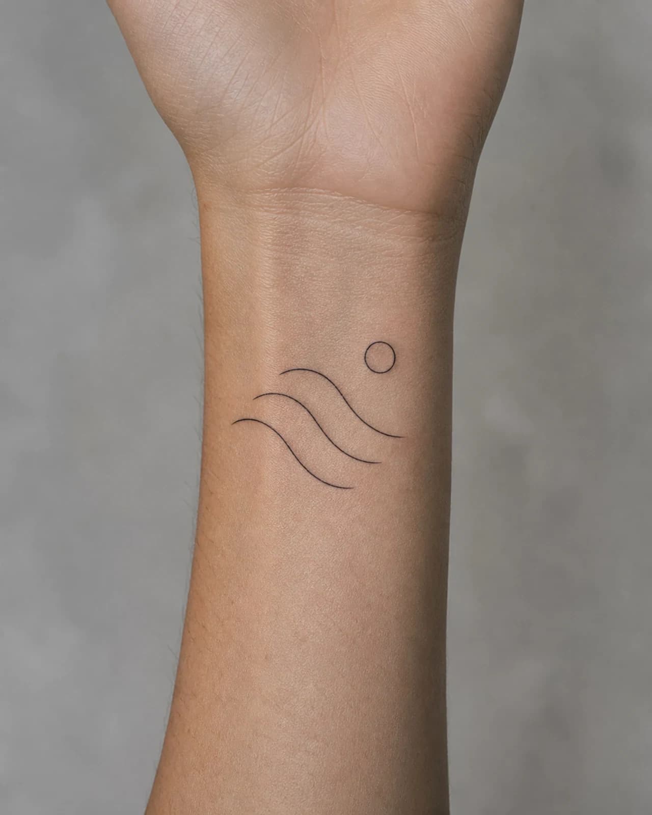 Abstract fine line tidal arcs and a small moon tattooed above an adult wrist