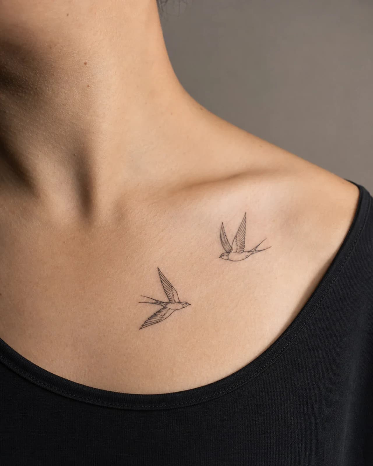 Two small fine line swallows in flight arranged across an adult collarbone